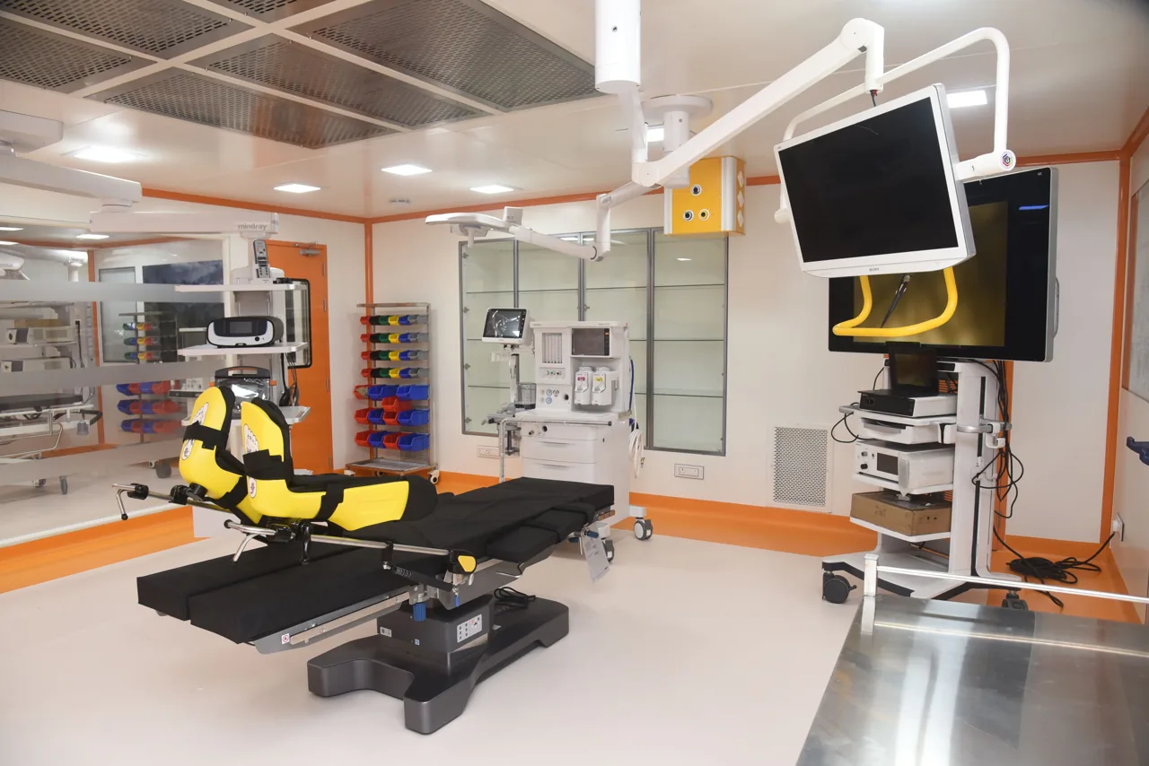 Operating theatre with a surgical table, overhead monitor and glass-fronted storage