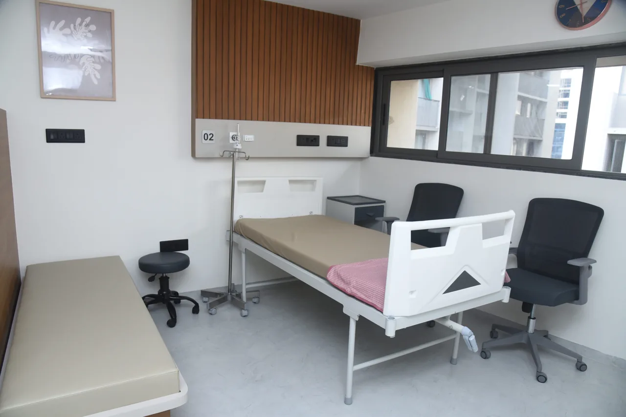 Hospital bed beside visitor chairs and a window